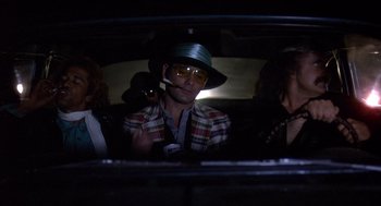 Movie still from “Where the Buffalo Roam” (1980), directed by Art Linson – A man with a hat smoking a cigarette in the back of a car; Medium shot, Low angle