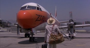 Movie still from “Where the Buffalo Roam” (1980), directed by Art Linson – A man in a hat is holding a bag and looking at a plane; Wide shot, High angle