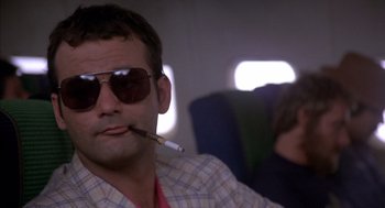 Movie still from “Where the Buffalo Roam” (1980), directed by Art Linson – A man smoking a cigarette while sitting on an airplane; Close Up shot, Low angle