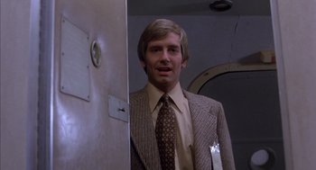 Movie still from “Where the Buffalo Roam” (1980), directed by Art Linson – A man wearing a suit and tie standing in front of a door; Medium shot, Low angle