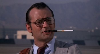 Movie still from “Where the Buffalo Roam” (1980), directed by Art Linson – A man in a suit and tie smoking a cigarette; Close Up shot, Low angle