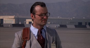 Movie still from “Where the Buffalo Roam” (1980), directed by Art Linson – A man in a suit and tie standing on a runway; Close Up shot, Low angle