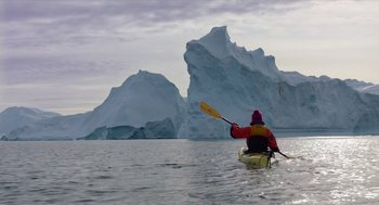 Movie still from “Where'd You Go, Bernadette” (2019), directed by Richard Linklater – A person in a kayak in the water with a large iceberg in the background; Extreme Wide shot, Low angle