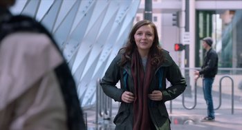 Movie still from “Where'd You Go, Bernadette” (2019), directed by Richard Linklater – A woman in a green jacket standing on a sidewalk; Medium shot, Over the shoulder angle
