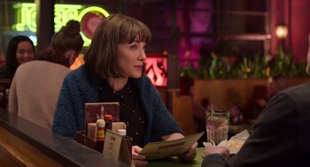 Movie still from “Where'd You Go, Bernadette” (2019), directed by Richard Linklater – A woman sitting at a table in front of a drink; Medium shot, Over the shoulder angle