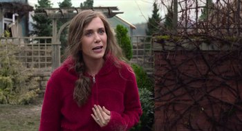Movie still from “Where'd You Go, Bernadette” (2019), directed by Richard Linklater – A woman in a red jacket standing in front of a brick wall; Medium shot, Over the shoulder angle