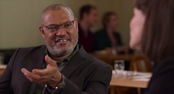 Movie still from “Where'd You Go, Bernadette” (2019), directed by Richard Linklater – An older man sitting at a table in front of a group of people; Close Up shot, Over the shoulder angle