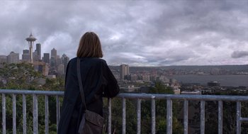 Movie still from “Where'd You Go, Bernadette” (2019), directed by Richard Linklater – A woman standing on top of a metal railing looking at a city skyline; Extreme Wide shot, Over the shoulder angle