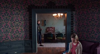 Movie still from “Where'd You Go, Bernadette” (2019), directed by Richard Linklater – A man standing in a doorway with a woman sitting in the background; Wide shot, Over the shoulder angle