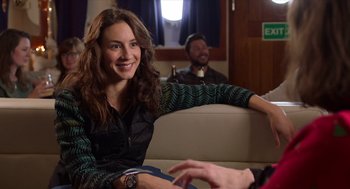 Movie still from “Where'd You Go, Bernadette” (2019), directed by Richard Linklater – A woman sitting on top of a couch next to a man; Medium shot, Over the shoulder angle