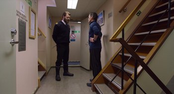 Movie still from “Where'd You Go, Bernadette” (2019), directed by Richard Linklater – Two men standing next to each other in front of stairs; Wide shot, Over the shoulder angle
