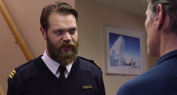 Movie still from “Where'd You Go, Bernadette” (2019), directed by Richard Linklater – A man with a long beard and mustache wearing a uniform; Close Up shot, Over the shoulder angle