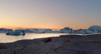 Movie still from “Where'd You Go, Bernadette” (2019), directed by Richard Linklater – Two people are laying on the rocks near the water; Extreme Wide shot, High angle
