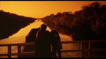Movie still from “While You Were Sleeping” (1995), directed by Jon Turteltaub – Two people standing on a bridge over a river at sunset; Extreme Wide shot, Over the shoulder angle