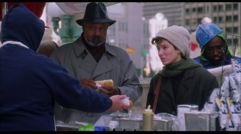 Movie still from “While You Were Sleeping” (1995), directed by Jon Turteltaub – A man and a woman eating a hot dog at an outdoor market; Medium shot, Over the shoulder angle