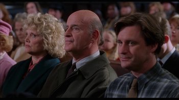 Movie still from “While You Were Sleeping” (1995), directed by Jon Turteltaub – A man and a woman sitting next to each other in front of other people; Medium shot, Over the shoulder angle