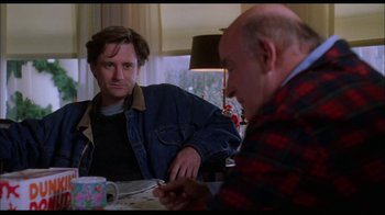 Movie still from “While You Were Sleeping” (1995), directed by Jon Turteltaub – Two men are sitting at a table and one of the men is looking at the other man; Medium shot, Over the shoulder angle