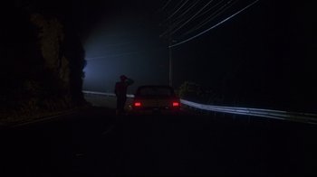 Movie still from “White Dog” (1982), directed by Samuel Fuller – A man standing on the side of a road next to a car; Extreme Wide shot, Low angle