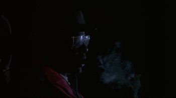 Movie still from “White Dog” (1982), directed by Samuel Fuller – A man wearing a hat and glasses smoking a cigarette; Close Up shot, Low angle
