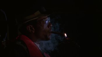 Movie still from “White Dog” (1982), directed by Samuel Fuller – A man in a hat and glasses is smoking a cigar; Close Up shot, Low angle