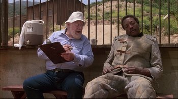 Movie still from “White Dog” (1982), directed by Samuel Fuller – A man sitting next to another man on a bench; Medium shot, High angle