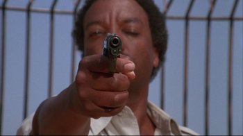 Movie still from “White Dog” (1982), directed by Samuel Fuller – A man holding a gun in front of a fence; Close Up shot, Low angle