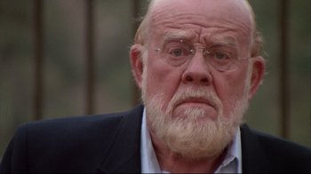 Movie still from “White Dog” (1982), directed by Samuel Fuller – An older man with a beard and glasses; Close Up shot, Over the shoulder angle