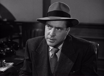 Movie still from “White Heat” (1949), directed by Raoul Walsh – A man wearing a suit and a hat is sitting down; Close Up shot, Low angle