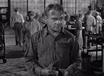 Movie still from “White Heat” (1949), directed by Raoul Walsh – An old photo of a man holding a book in front of other men; Medium shot, Over the shoulder angle