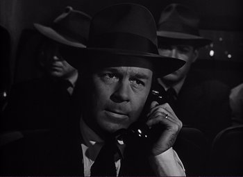 Movie still from “White Heat” (1949), directed by Raoul Walsh – A man in a suit and hat talking on a phone; Close Up shot, Low angle