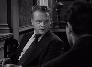 Movie still from “White Heat” (1949), directed by Raoul Walsh – A man wearing a suit and tie sitting in front of another man in a suit; Close Up shot, Over the shoulder angle