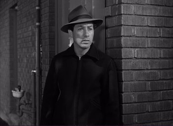 Movie still from “White Heat” (1949), directed by Raoul Walsh – A man wearing a hat standing in front of a brick wall; Medium shot, Low angle