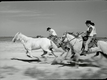 Movie still from “White Mane” (1953), directed by Albert Lamorisse – Two men on horses are running through the desert; Wide shot, Low angle