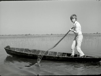 Movie still from “White Mane” (1953), directed by Albert Lamorisse – A young boy paddling a boat in the middle of a lake; Wide shot, High angle