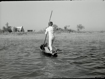 Movie still from “White Mane” (1953), directed by Albert Lamorisse – A man is standing on a boat in the middle of a lake; Wide shot, High angle