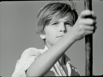 Movie still from “White Mane” (1953), directed by Albert Lamorisse – A young boy holding onto a wooden pole; Close Up shot, Low angle