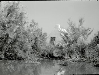 Movie still from “White Mane” (1953), directed by Albert Lamorisse – A black - and - white photo of a house near a body of water; Extreme Wide shot, Low angle