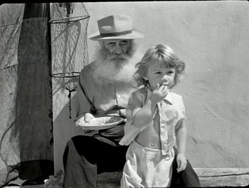 Movie still from “White Mane” (1953), directed by Albert Lamorisse – An old man sitting next to a little girl; Medium shot, High angle