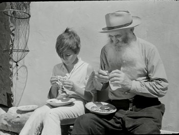 Movie still from “White Mane” (1953), directed by Albert Lamorisse – An older man and a young boy eating food; Medium shot, High angle