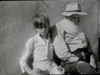 Movie still from “White Mane” (1953), directed by Albert Lamorisse – An older man sitting next to a young boy; Medium shot, High angle