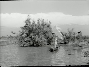 Movie still from “White Mane” (1953), directed by Albert Lamorisse – A woman is paddling a canoe down a river; Extreme Wide shot, Low angle