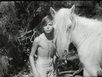 Movie still from “White Mane” (1953), directed by Albert Lamorisse – A young boy standing next to a white horse; Medium shot, High angle