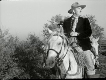 Movie still from “White Mane” (1953), directed by Albert Lamorisse – A man riding a white horse with trees in the background; Medium shot, Low angle