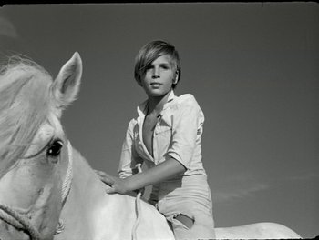 Movie still from “White Mane” (1953), directed by Albert Lamorisse – A young woman sitting on the back of a white horse; Medium shot, Low angle