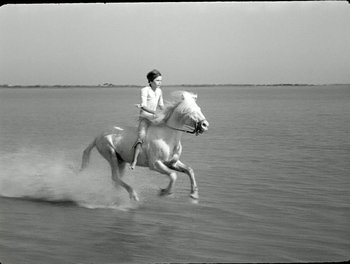 Movie still from “White Mane” (1953), directed by Albert Lamorisse – A man riding on the back of a white horse through the water; Wide shot, High angle