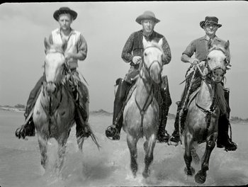Movie still from “White Mane” (1953), directed by Albert Lamorisse – A group of men riding horses on a beach; Wide shot, Low angle