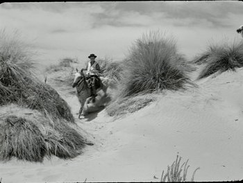 Movie still from “White Mane” (1953), directed by Albert Lamorisse – A man riding on the back of a horse through the sand; Wide shot, High angle