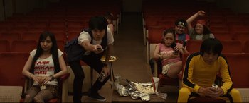 Movie still from “Why Don't You Play in Hell?” (2013), directed by Sion Sono – A man and a woman sitting in front of a pile of food; Wide shot, High angle