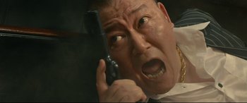 Movie still from “Why Don't You Play in Hell?” (2013), directed by Sion Sono – A man holding a cell phone up to his face; Close Up shot, Low angle