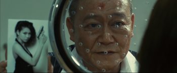 Movie still from “Why Don't You Play in Hell?” (2013), directed by Sion Sono – An older man looking into a mirror with a lot of beads on his face; Extreme Close Up shot, Low angle